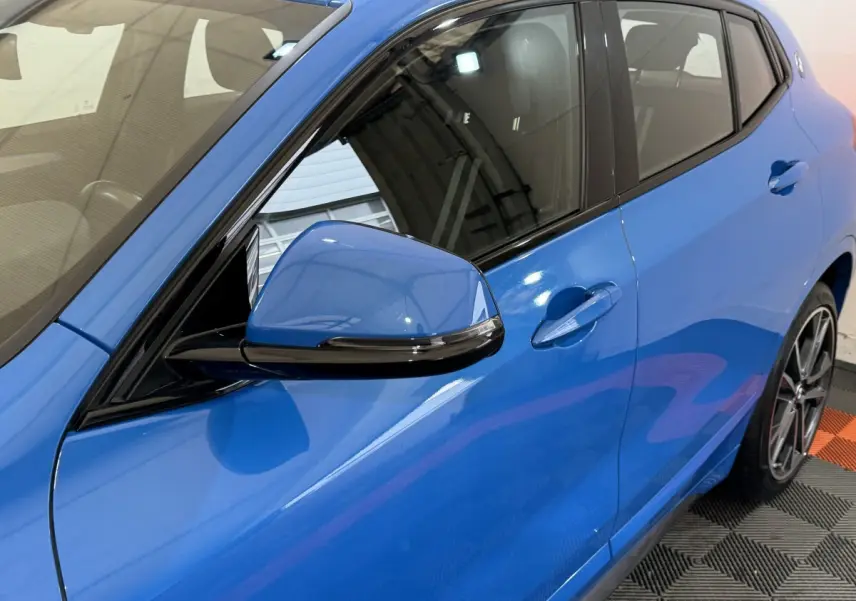 Vue côté gauche rapprochée du BMW X2 xDrive25e M Sport bleu, mettant en valeur la portière et le rétroviseur.