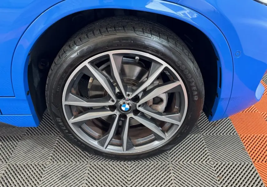 Gros plan sur la roue avant droite d’une BMW X2 bleu électrique, mettant en valeur la jante alliage moderne.