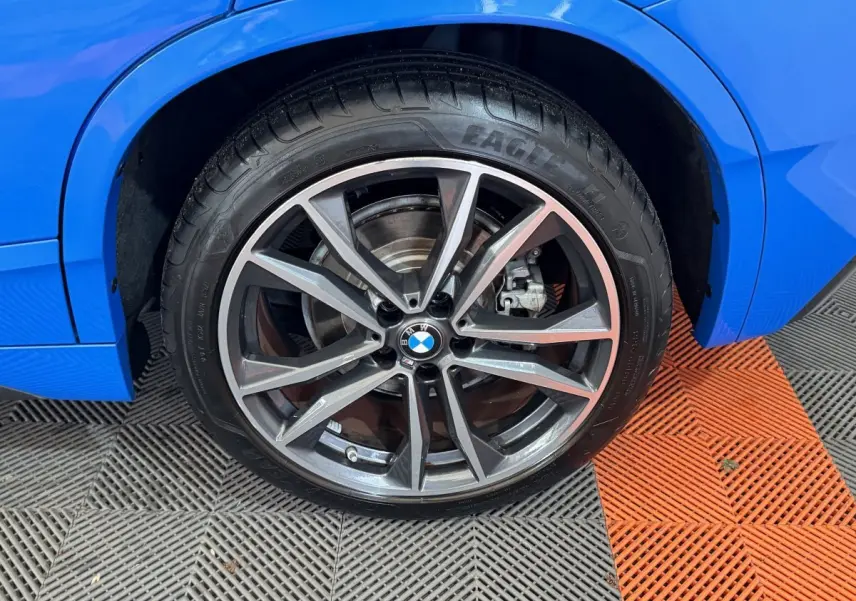 Gros plan sur la roue avant droite d’un BMW X2 bleu, avec jante alliage à branches doubles et logo BMW central.