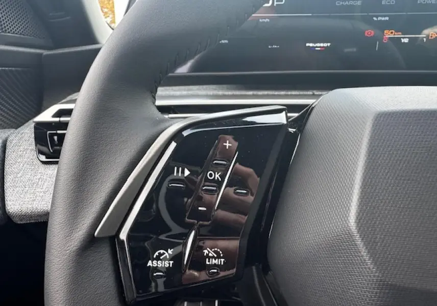 Gros plan sur les commandes gauche du volant cuir noir du Peugeot 5008 2025 avec tableau de bord numérique en arrière-plan.