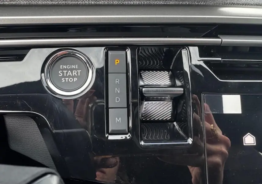 Gros plan sur la console centrale noire brillante du Peugeot 5008 Bleu Ingaro, avec bouton start/stop et commandes de boîte auto.