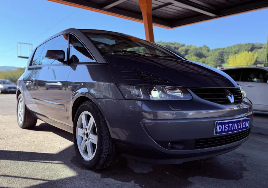 Renault Avantime gris en 3/4 avant droit sous abri, mettant en valeur ses phares allumés et sa silhouette unique.
