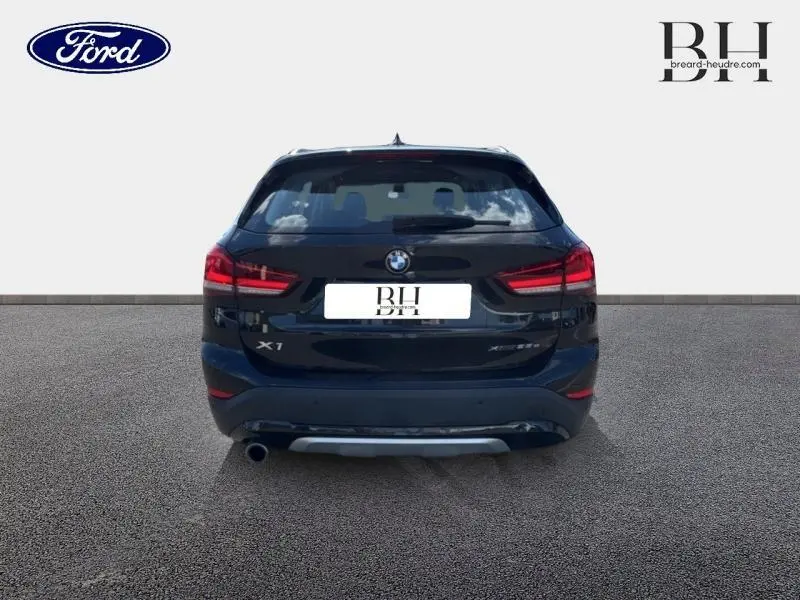 Vue arrière d'un BMW X1 xDrive25eA 220ch xLine 2021 en noir saphir, avec feux arrière LED et sortie d'échappement chromée.