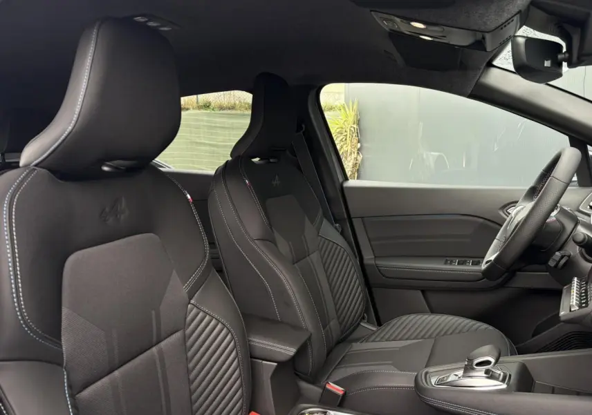 Vue intérieure côté droit du Renault Captur Esprit Alpine 2025, sièges noirs avec logo Alpine et volant surpiqué tricolore.