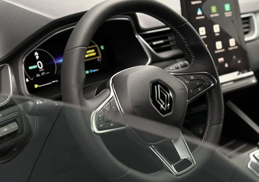 Gros plan sur le volant noir avec surpiqûres tricolores du Renault Captur 2025, tableau de bord numérique en arrière-plan.