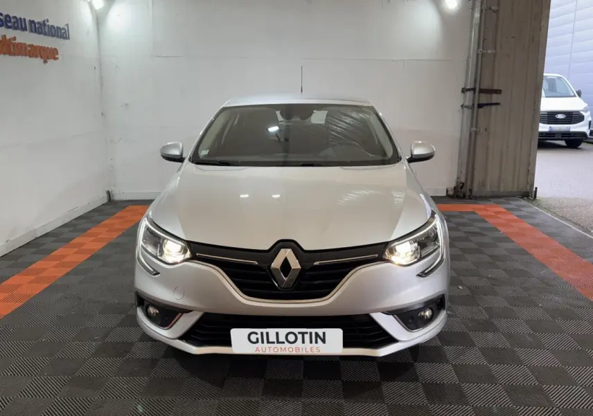 Vue avant d'une Renault Mégane Business gris clair avec phares allumés dans un garage éclairé.