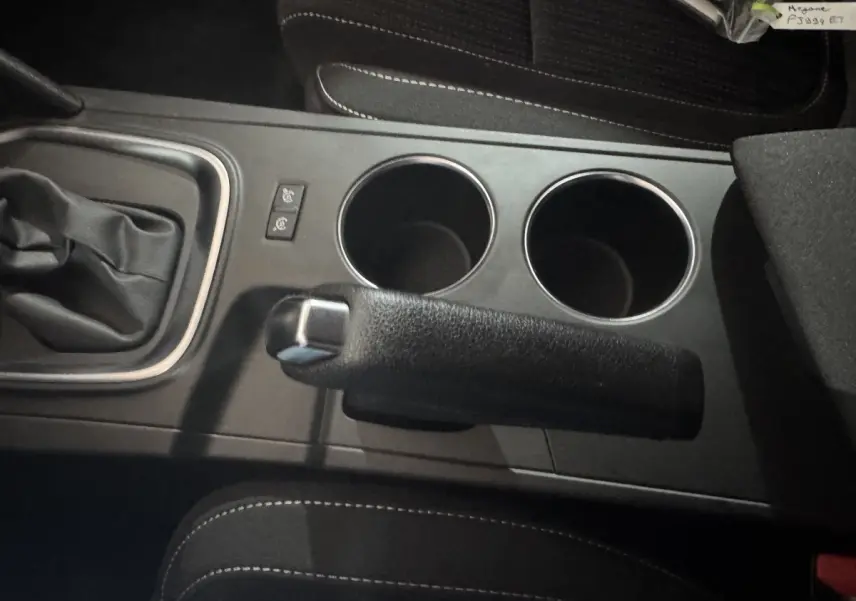 Vue rapprochée de la console centrale noire avec frein à main, deux porte-gobelets et levier de vitesse d’une Renault Mégane Business gris clair.