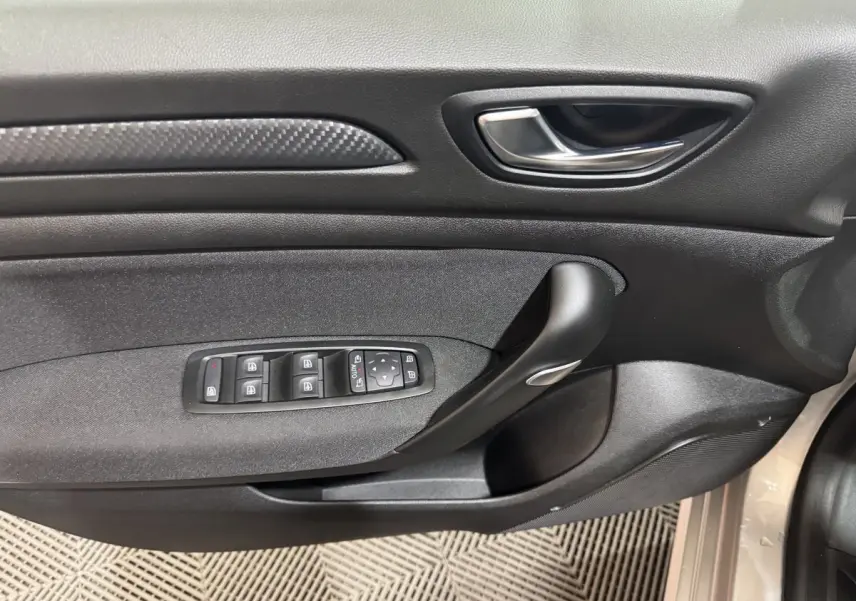 Gros plan sur la porte intérieure côté conducteur de la Renault Mégane gris clair, avec commandes des vitres et poignée noire.