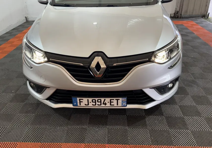 Vue avant d'une Renault Mégane gris clair avec phares allumés et calandre noire brillante.