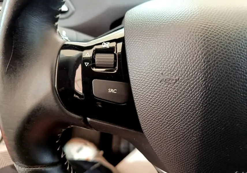 Gros plan sur le volant cuir noir de la Peugeot 308 avec commandes audio intégrées côté gauche.