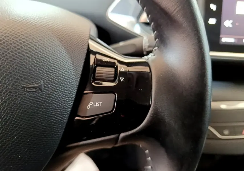 Gros plan sur les commandes du volant cuir noir de la Peugeot 308, avec écran tactile en arrière-plan.