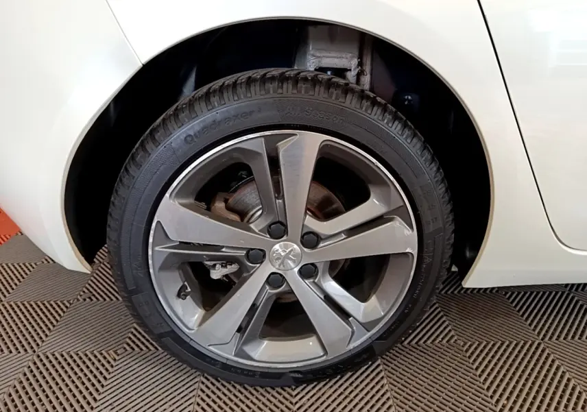 Gros plan sur la roue arrière droite d’une Peugeot 308 blanche, mettant en valeur la jante alliage grise au design moderne.