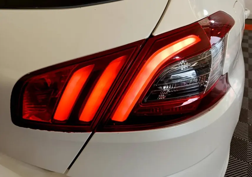 Gros plan sur le feu arrière droit rouge allumé d'une Peugeot 308 blanche, mettant en valeur ses trois griffes lumineuses.