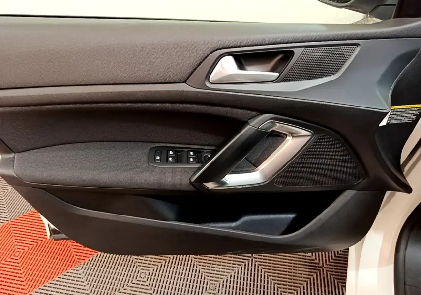 Vue rapprochée de la porte avant gauche noire de la Peugeot 308 blanche, avec poignée argentée et commandes de vitres.