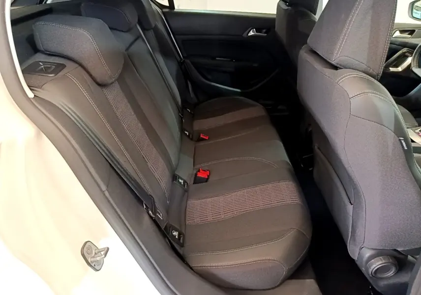 Vue intérieure côté arrière gauche de la banquette noire de la Peugeot 308 blanche, avec appuie-têtes et ceintures visibles.