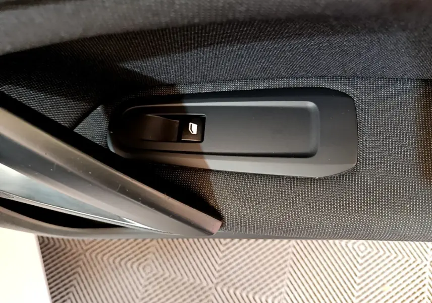 Gros plan sur la poignée de déverrouillage de porte intérieure noire sur tissu gris d'une Peugeot 308 blanche.