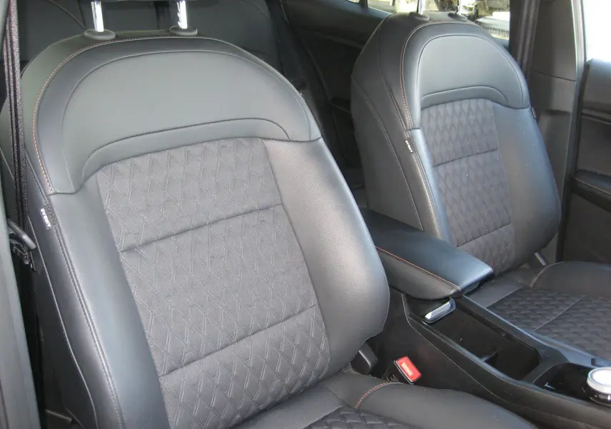 Gros plan sur les sièges avant en cuir noir et tissu gris avec surpiqûres orange dans l’habitacle du MG3 1.5 Hybrid Luxury 2025.
