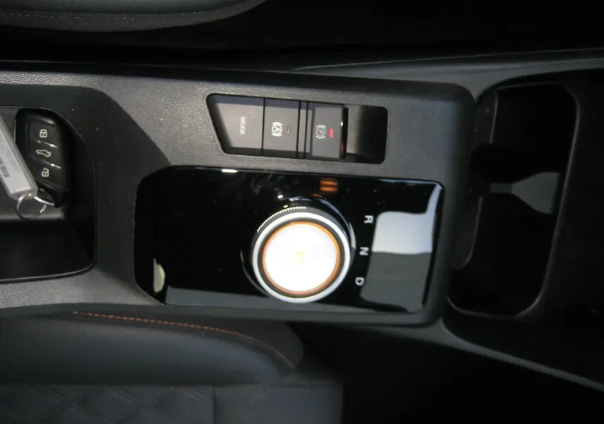 Gros plan sur la console centrale noire du MG3 1.5 Hybrid 2025 avec molette de boîte auto et boutons de frein à main électronique.