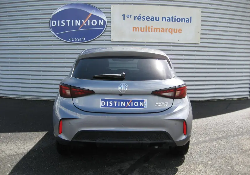 Vue arrière d'une MG3 1.5 Hybrid gris 2025 avec feux LED et logo MG bien visibles sur fond de mur métallique.