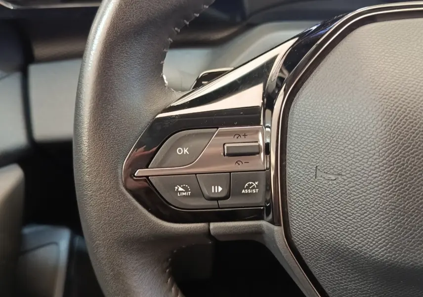 Gros plan sur le côté gauche du volant cuir noir de la Peugeot 308 avec commandes multifonctions visibles.