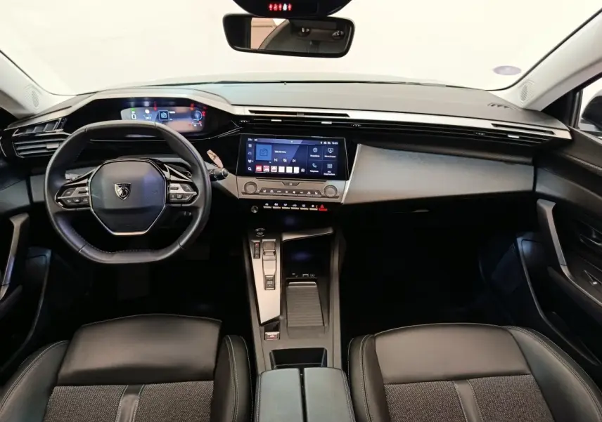 Vue intérieure avant de la Peugeot 308 2023, tableau de bord noir avec écran tactile central et volant cuir multifonctions.