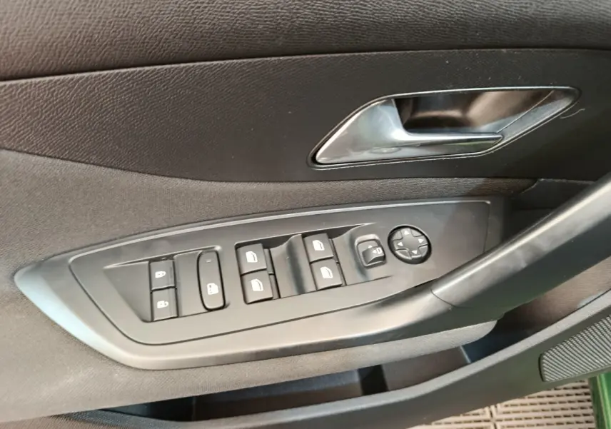 Détail des commandes de lève-vitres et rétroviseurs sur la porte côté conducteur d’une Peugeot 308 vert 2023.