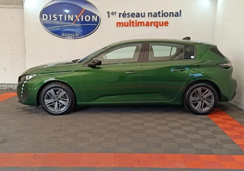 Peugeot 308 vert vue de profil côté gauche, avec jantes alliage et feux LED distinctifs, en intérieur showroom.