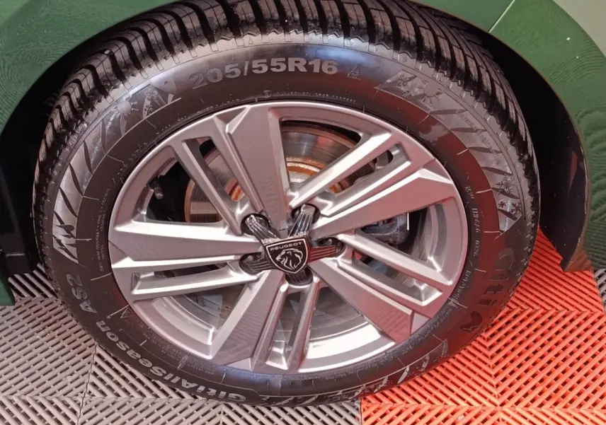 Gros plan sur la roue avant droite d'une Peugeot 308 vert 2023 avec jante alliage et logo lion central.
