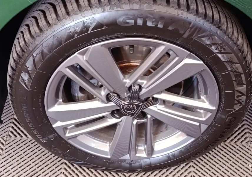 Gros plan sur la roue avant droite d'une Peugeot 308 verte, jante alliage à design moderne et logo lion central.