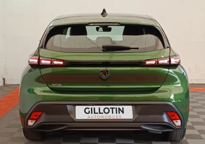 Vue arrière d’une Peugeot 308 2023 vert métallisé avec feux LED allumés et logo lion central sur hayon.