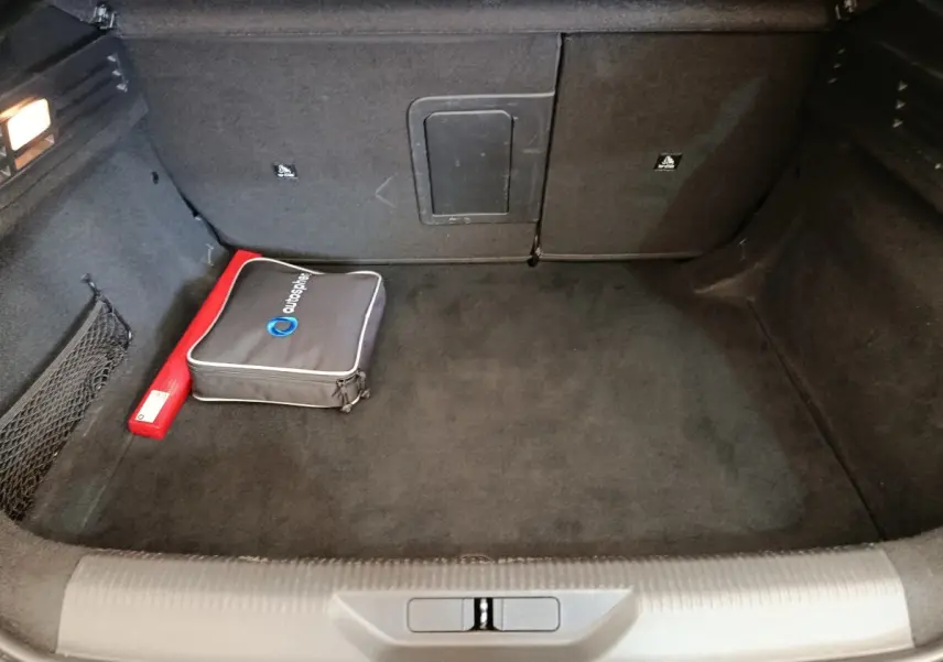 Coffre ouvert de la Peugeot 308 vert, vue intérieure montrant un rangement noir avec trousse et triangle de sécurité.