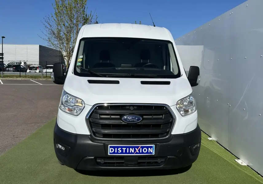 Vue frontale d'un fourgon Ford Transit blanc avec calandre noire et plaque Distinxion sur un parking extérieur.