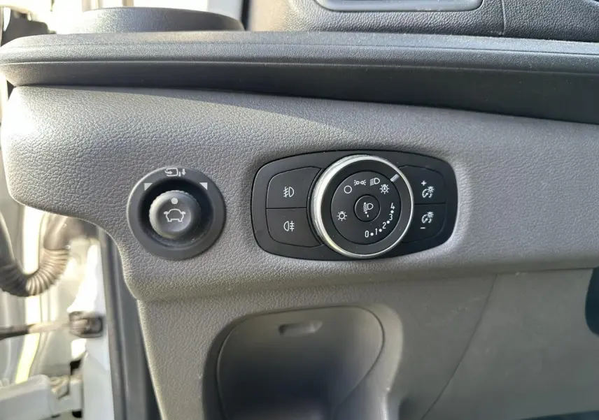 Gros plan sur les commandes d'éclairage et de réglage des rétroviseurs du Ford Transit Fourgon blanc, côté conducteur.