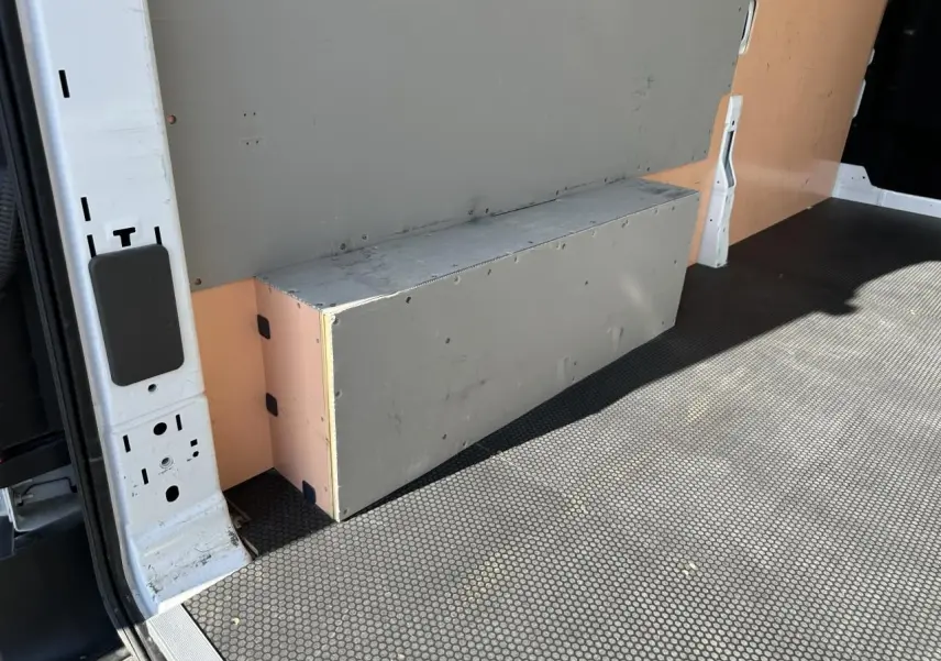 Détail de l'intérieur du fourgon Ford Transit blanc, montrant le revêtement et un caisson gris côté gauche.