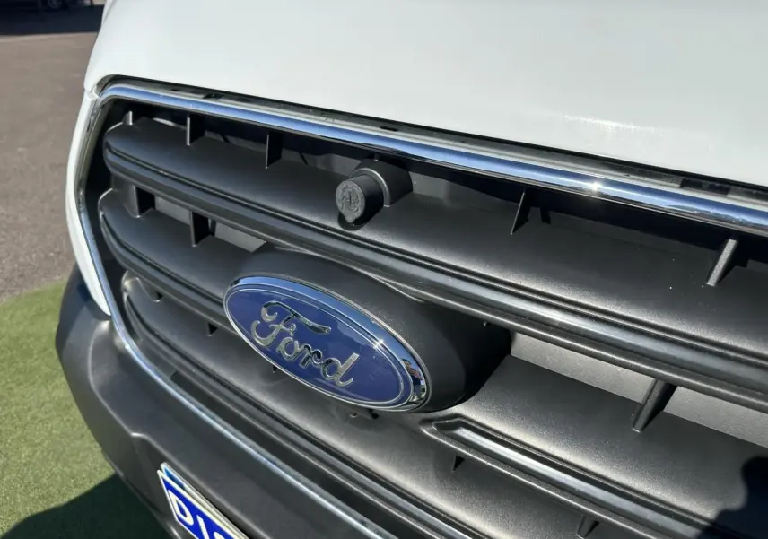 Gros plan sur la calandre noire avec logo Ford bleu et carrosserie blanche du Ford Transit Fourgon 2020.