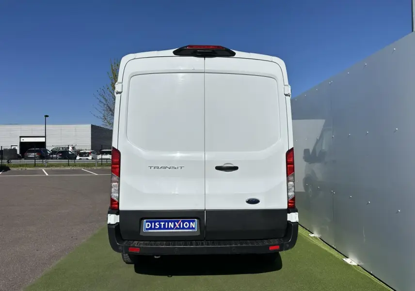 Vue arrière d'un fourgon Ford Transit blanc avec porte double et pare-chocs noir sous un ciel bleu.