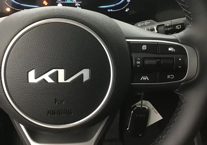 Gros plan sur le volant noir en cuir du Kia Sportage 2025 avec commandes intégrées et logo moderne au centre.