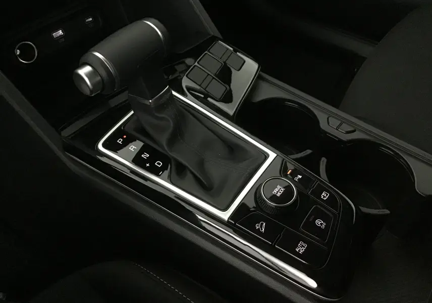 Gros plan sur la console centrale du Kia Sportage noir 2025, mettant en valeur le levier de vitesses automatique et les commandes de conduite.