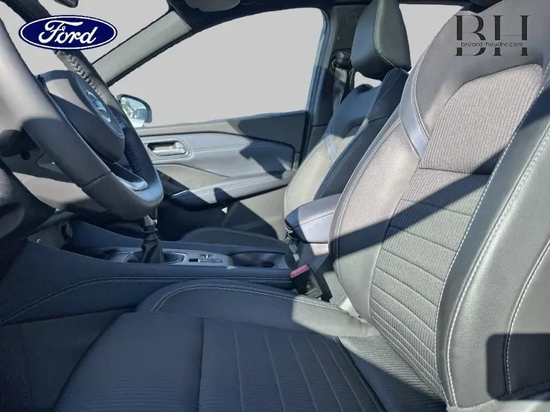 Vue intérieure côté conducteur montrant les sièges noirs en cuir et tissu avec volant et levier de vitesse manuelle.