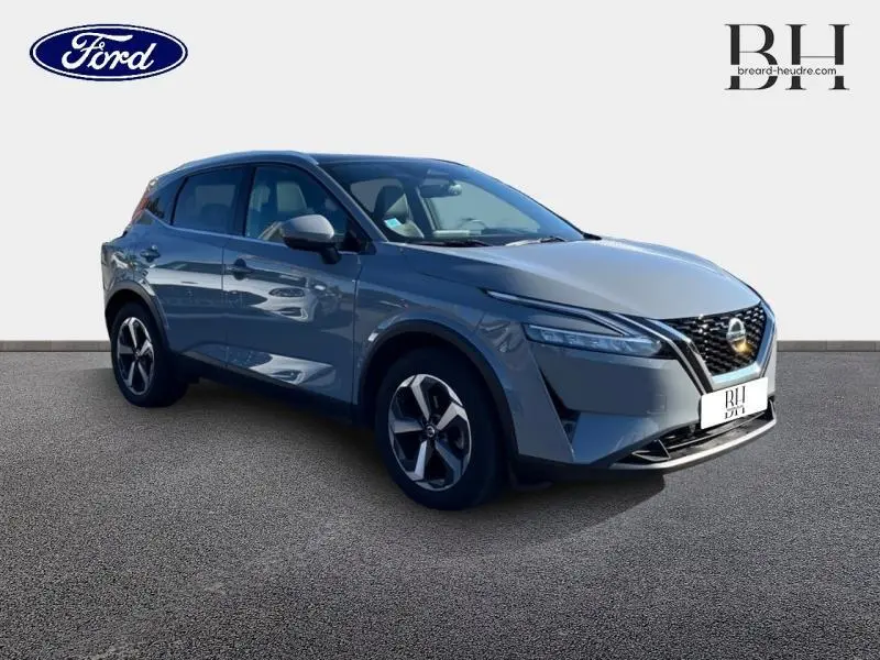 Nissan Qashqai 1.3 Mild Hybrid gris Argile vue 3/4 avant droit avec calandre noire et jantes alu distinctives.