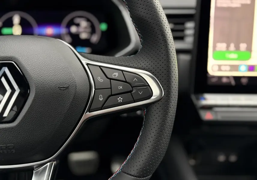 Gros plan sur le volant perforé du Renault Captur blanc nacré 2025 avec commandes intégrées et surpiqûres tricolores.