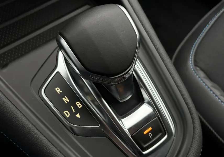 Gros plan sur le levier de vitesses noir et chrome de la Renault Captur hybride, avec surpiqûres bleues visibles sur la sellerie.