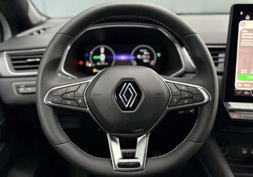 Volant noir perforé avec logo Renault, vue frontale sur tableau de bord numérique et écran tactile latéral.
