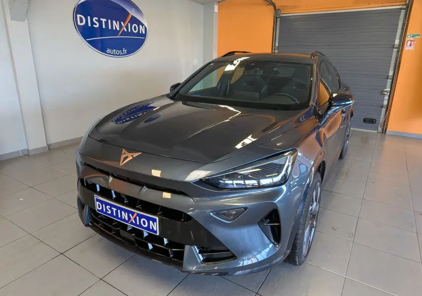 Vue 3/4 avant d'une CUPRA Formentor gris magnétique métal avec logo cuivré, dans un showroom intérieur.