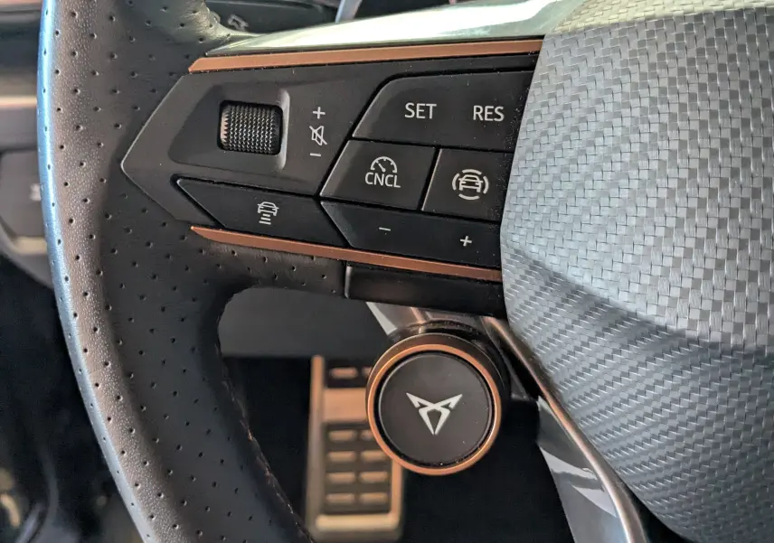 Gros plan sur le volant perforé noir avec commandes multifonctions et logo CUPRA en finition cuivre.