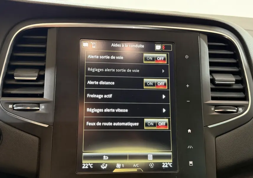 Écran tactile central de la Renault Mégane Intens gris foncé, affichant les aides à la conduite, entouré de grilles d’aération.