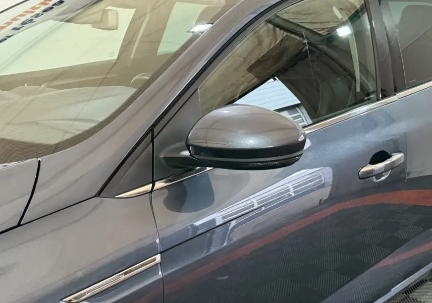 Détail du côté gauche d’une Renault Mégane gris foncé, montrant la portière et le rétroviseur extérieur.