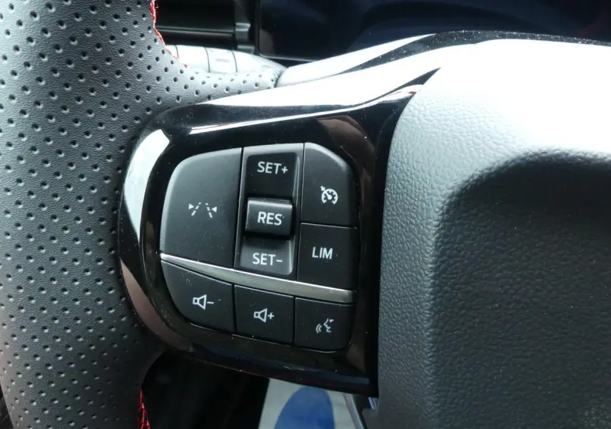 Gros plan sur les commandes du volant perforé noir du Ford Puma 2025, avec boutons de régulateur et volume sonore.