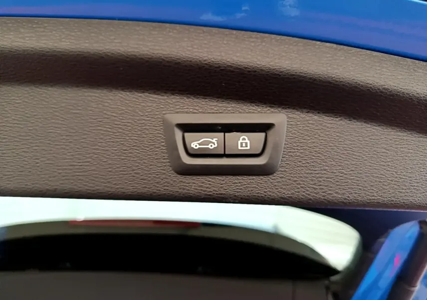 Gros plan sur le bouton d'ouverture et de verrouillage du coffre, intérieur du hayon bleu du BMW X2 sDrive20i M Sport.
