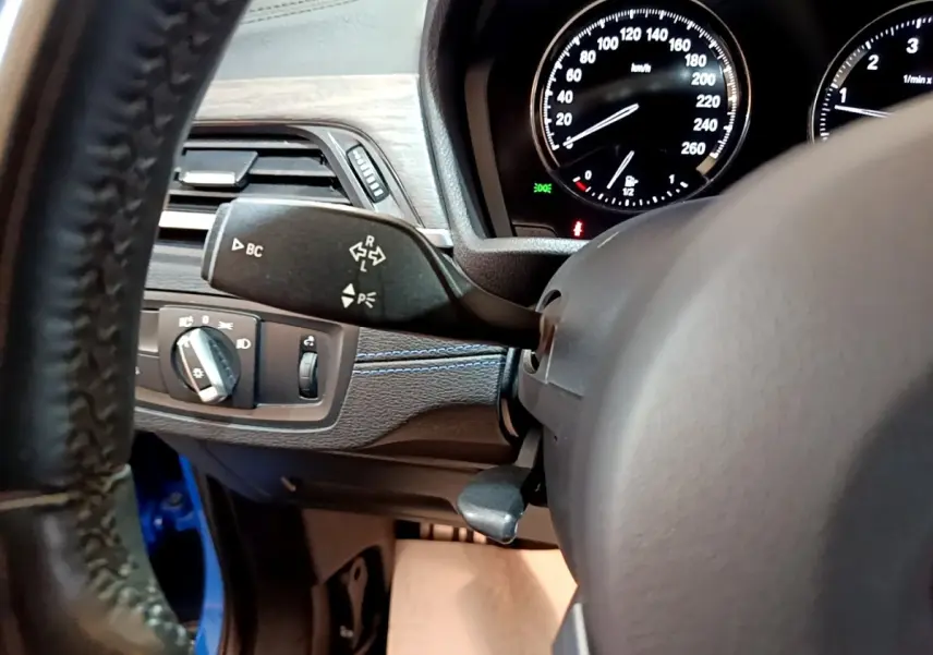 Détail intérieur côté gauche du tableau de bord BMW X2 bleu, avec commandes des phares et compteurs visibles.